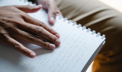 Imagen de manos leyendo escritura Braille en cuaderno anillado
